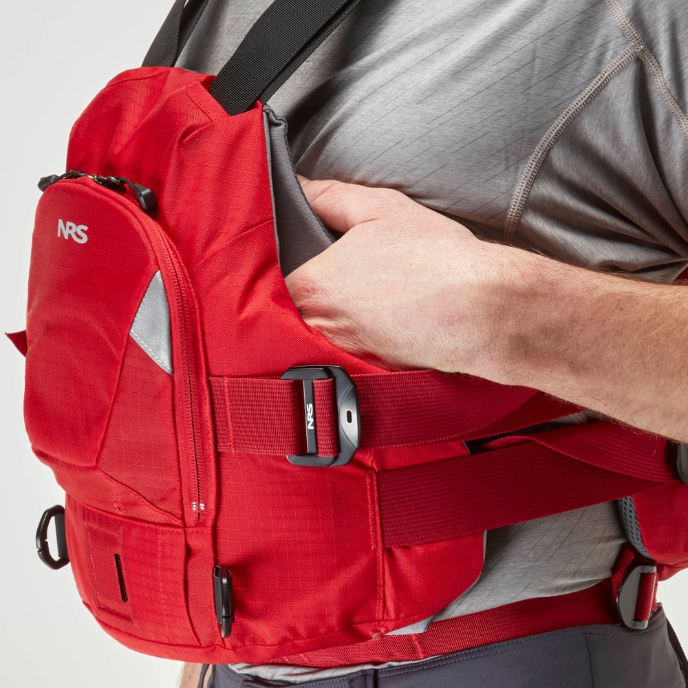 A person in a red NRS Ninja Pro PFD over a gray shirt adjusts the side strap, showcasing this rescue vest's secure fit—ideal for whitewater paddlers seeking reliable performance.