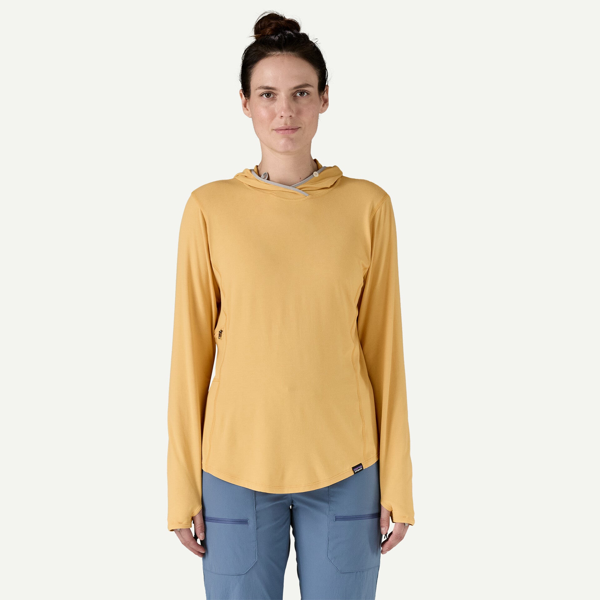 A woman wearing a Patagonia Tropic Comfort Natural Hoody in yellow and blue pants stands against a plain background.