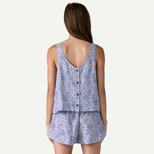 A person wearing the Garden Island Top by Patagonia, which is a light blue floral-patterned sleeveless top with a row of buttons down the back, paired with shorts, viewed from behind.