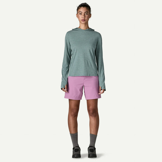 A person stands facing forward wearing a Patagonia Cap Cool Sun Hoody W's in light green, paired with lavender shorts, gray socks, and black shoes against a plain white background.