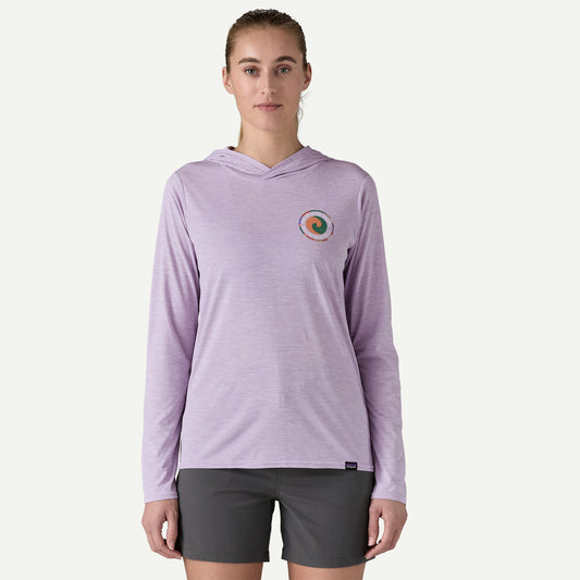 The person wears a Patagonia Cap Cool Daily Graphic Hoody - Women's in light purple with a small chest logo, paired with dark gray shorts made of recycled polyester, perfectly complementing the plain background.