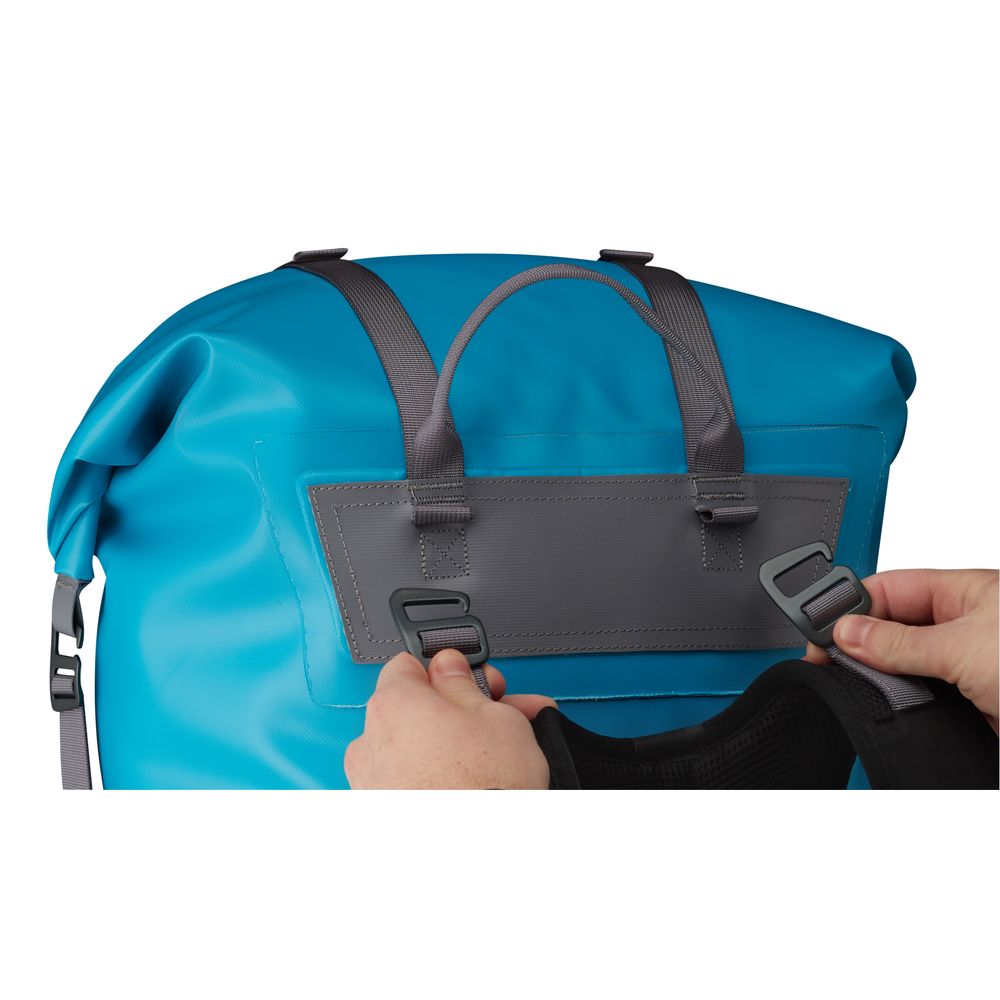 Hands securing the black compression straps on an NRS Bill's Bag, a blue waterproof backpack featuring gray buckles and shoulder straps.