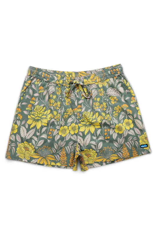 The Kavu Nosara Short by Kavu features green swim trunks with a yellow floral pattern, an elastic waistband with drawstring, and a small blue patch near the right hem.