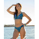 A woman in a Cardiff Reversible Bottom bikini by Carve stands on a boat, shielding her eyes and gazing into the distance over the water.