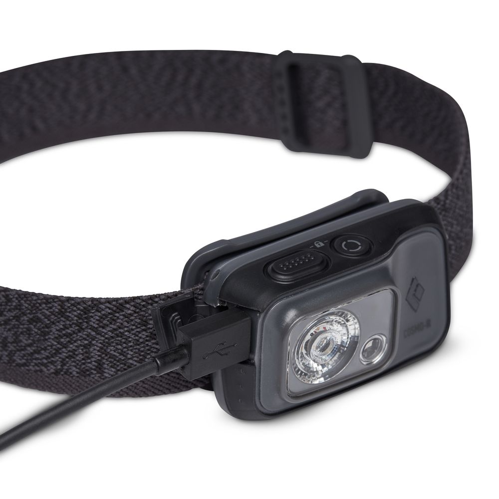The Black Diamond Cosmo 350R Rechargeable Headlamp in black is shown with its adjustable strap, being charged via a USB cable connected to a side port.