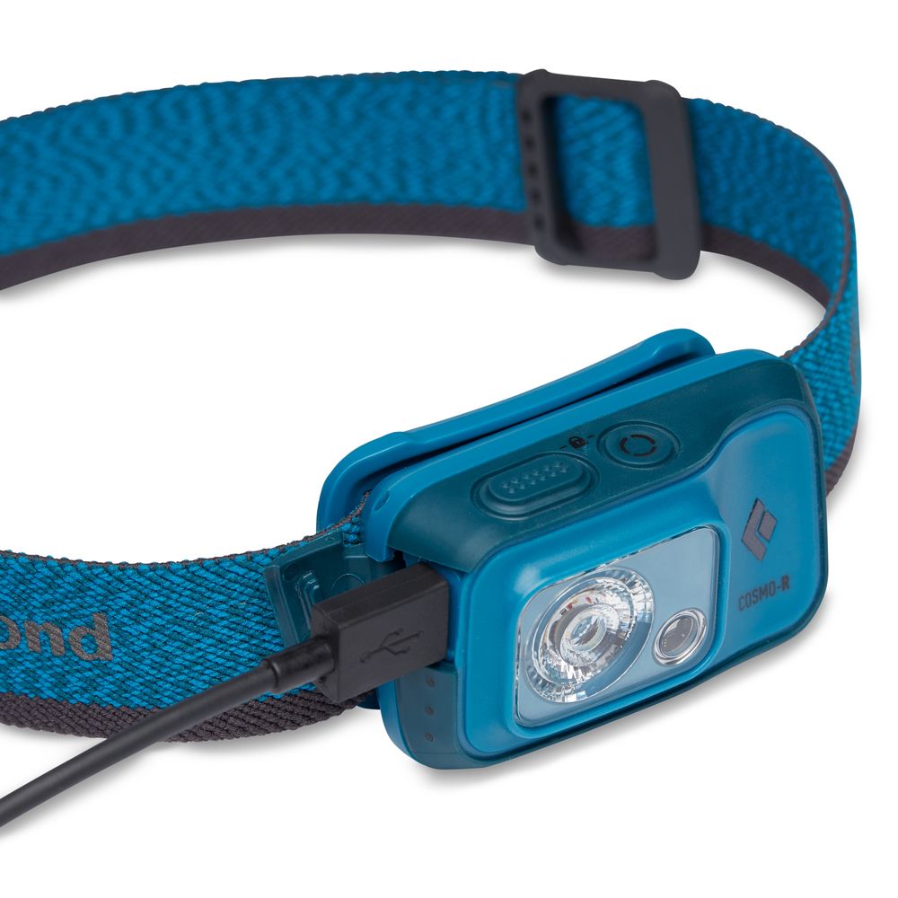 The Black Diamond Cosmo 350R Rechargeable Headlamp, featuring a blue and black design with a head strap, is being charged via USB—ideal for night vision activities.