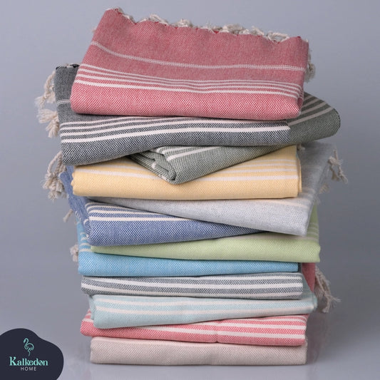A stack of colorful 4Corners Riversports Turkish Towels, featuring stripes in pink, gray, yellow, blue, green, and white, is neatly displayed on a flat surface.
