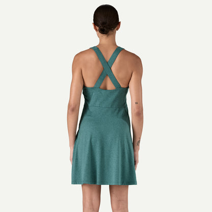 A person in the Seabrook Dress by Patagonia, a teal sleeveless design featuring crisscross straps, stands against a plain background with their back to the camera.