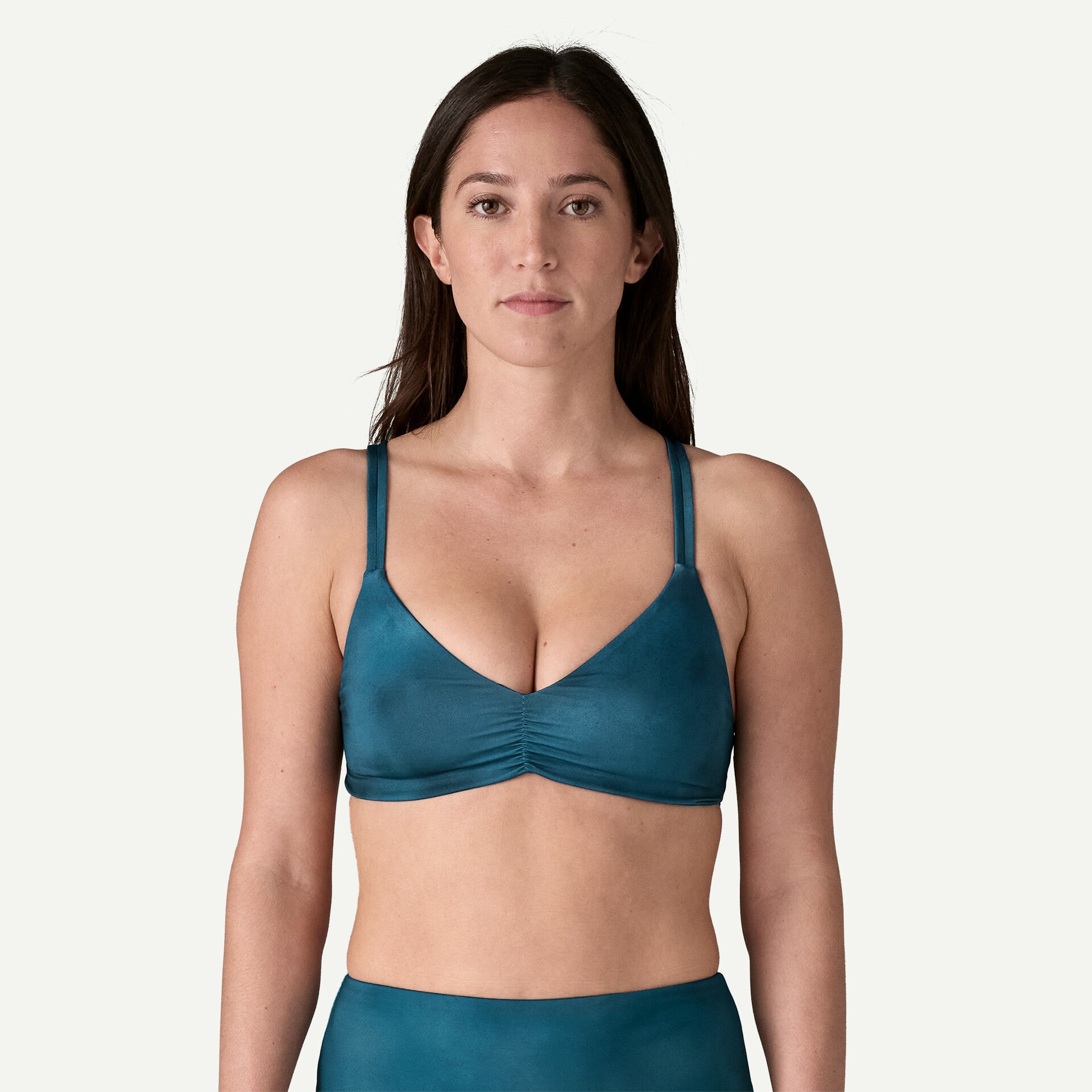 A person with long hair is wearing the Reversible Seaglass Bay Top in teal by Patagonia and facing forward against a plain background.