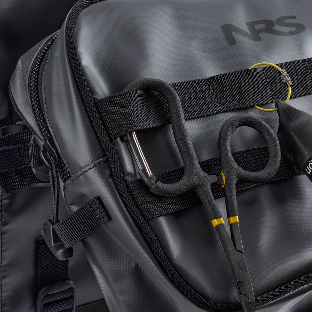 Black hemostat scissors clipped to the strap of the gray NRS Throw Back Fishing Seat Bag, showing a close-up of its PVC-free mesh material and rugged fastenings.
