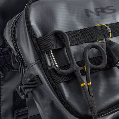 Black hemostat scissors clipped to the strap of the gray NRS Throw Back Fishing Seat Bag, showing a close-up of its PVC-free mesh material and rugged fastenings.