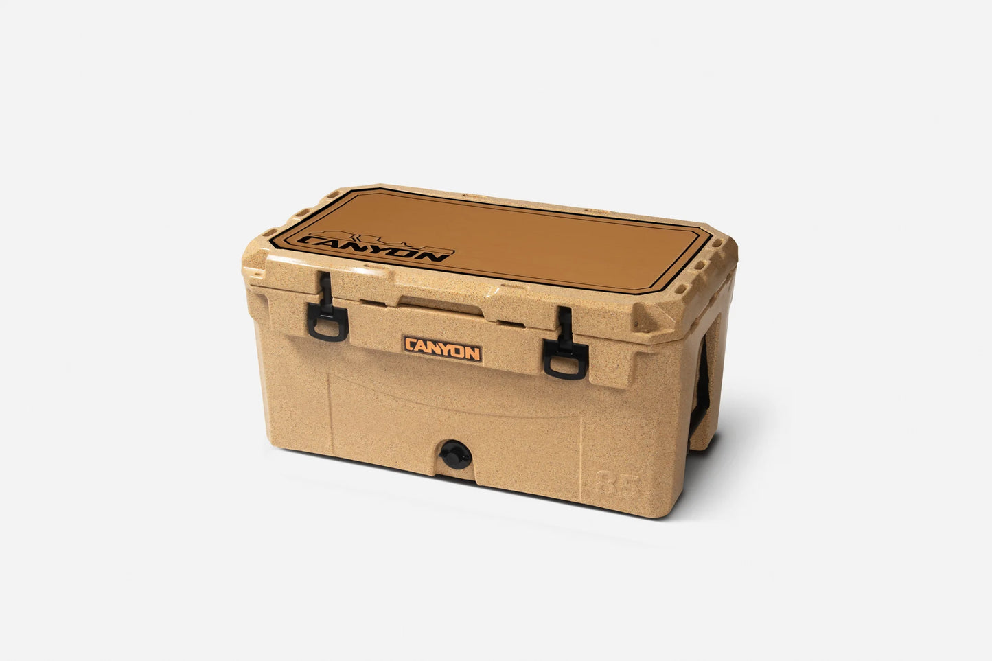 A tan hard plastic cooler with black latches and handles features a Canyon Coolers Cooler Traction Pad made of EVA foam, labeled "Canyon" on the lid and front, shown against a plain white background.