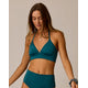 A woman models the Carve Dahlia Top, a teal halter bikini top with high-waisted bottoms, offering a flattering fit and comfortable design, set against a plain beige background.