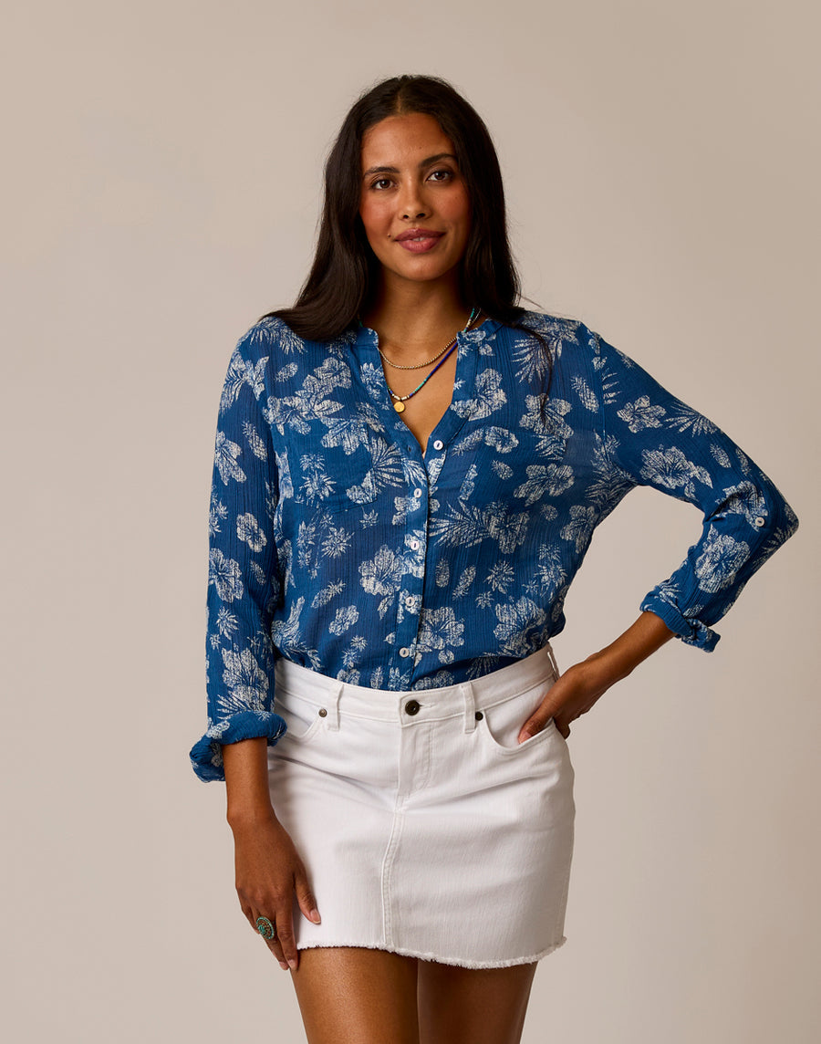 A woman stands against a plain background, wearing the Carve Dylan Gauze Tunic and a white denim skirt, with one hand on her hip.