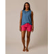 A woman stands barefoot on a neutral background, wearing a blue sleeveless top and bright pink Carve Oahu 4" Shorts made from stretch cotton corduroy.