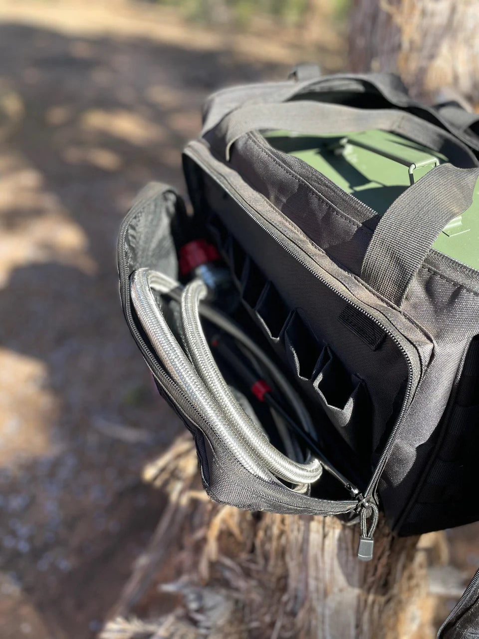 A BugOut Bag for LavaBox is hanging on a tree trunk near a grill.