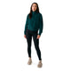 A woman stands against a white background wearing the Lole Yonder Half Zip in teal, black leggings, and beige sneakers.