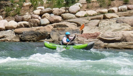 A person Senior Outdoor Inflatable Kayak+ing down a river with rocks in the background, embracing the beauty of their water reading+ experience.