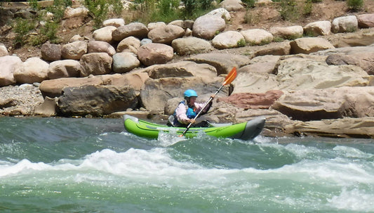 A person Senior Outdoor Inflatable Kayak+ing down a river with rocks in the background, embracing the beauty of their water reading+ experience.