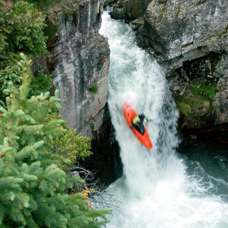 a man in an orange kayak is in a waterfall.