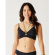 A woman with long dark hair smiles in front of a plain light background, wearing the Carve Elba Top bralette bikini by Carve with adjustable straps and layered necklaces.
