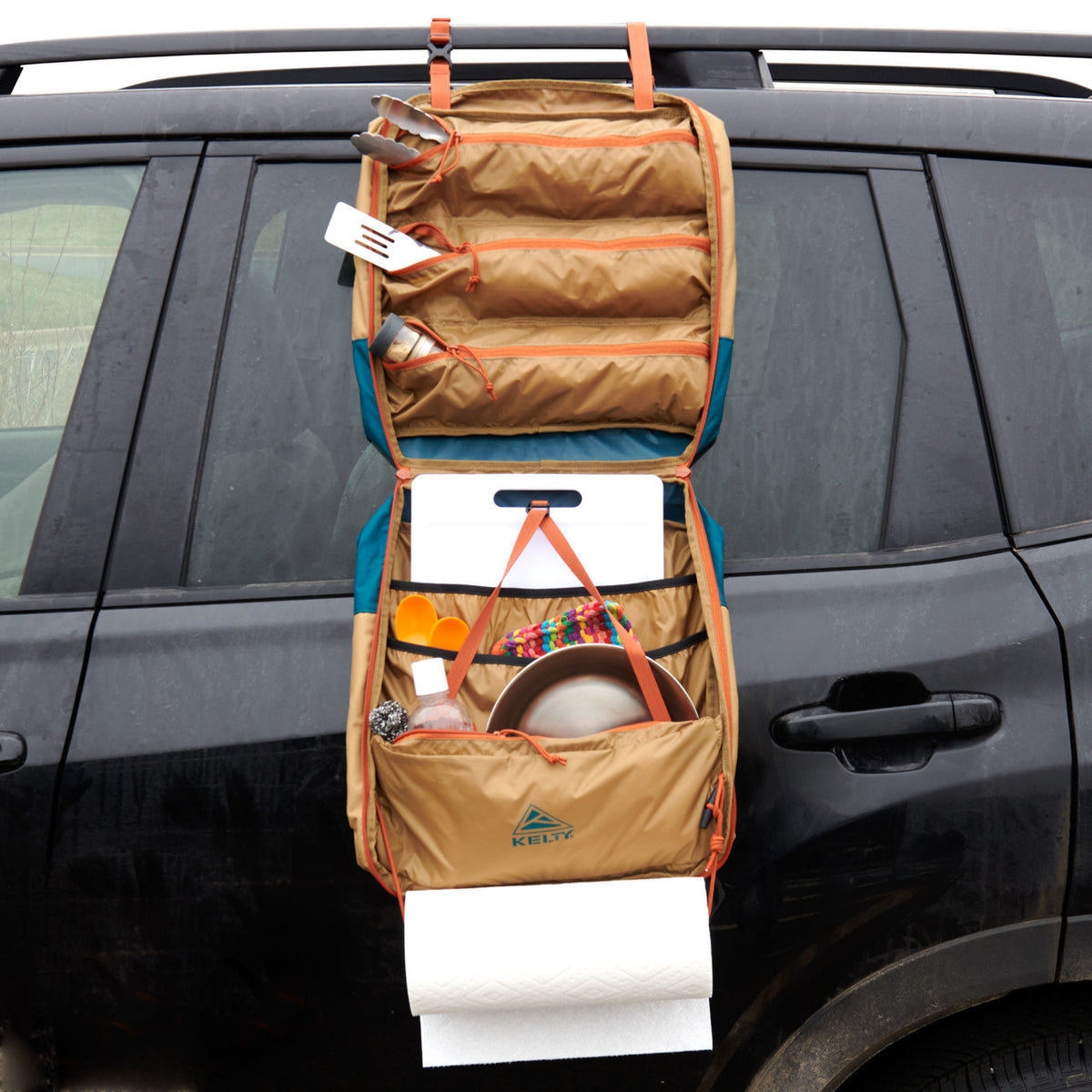 The Kelty Camp Galley hangs open on your car door, neatly displaying utensils, dishes, cups, and paper towels for easy access and organization at your campsite.