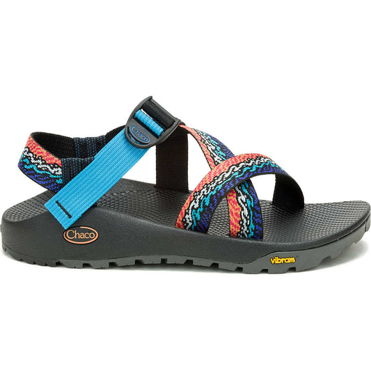 A side view shows the Chaco Z1 Rapid Pro - Men's sandal, featuring a black Vibram outsole, colorful patterned straps, and a blue adjustable ankle strap.