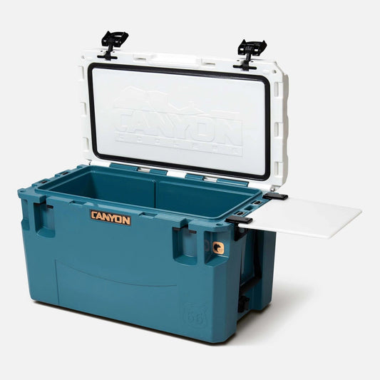 The blue and white PRO Series Coolers by Canyon Coolers, engineered for max ice retention, include a removable cutting board stored on the side when the lid is open. Rest easy with their lifetime warranty.