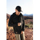 A person wearing a Castleton Grid Hoodie M's by Desert Wild zips up their jacket in a rocky desert landscape under a bright sky.
