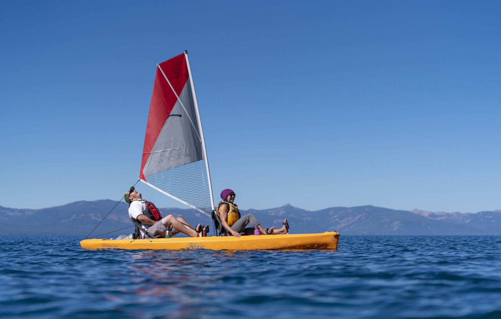 Two people on a Hobie Mirage Compass Duo 13'6 sailboat in the water.