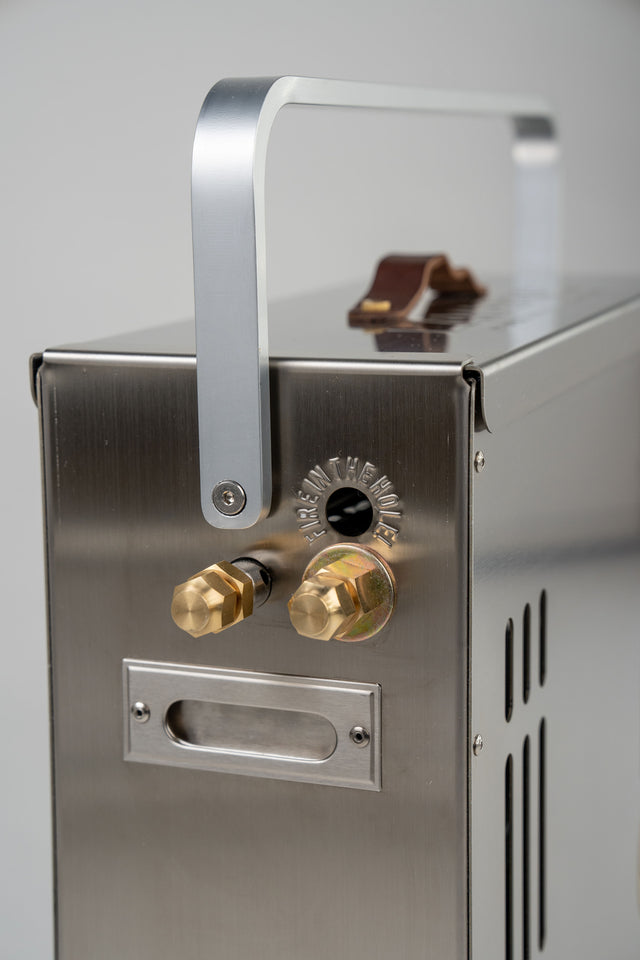 Close-up of the LavaBox BoomBox Portable Campfire, featuring a stainless steel body, metal handle, two brass fittings, and side ventilation slots.
