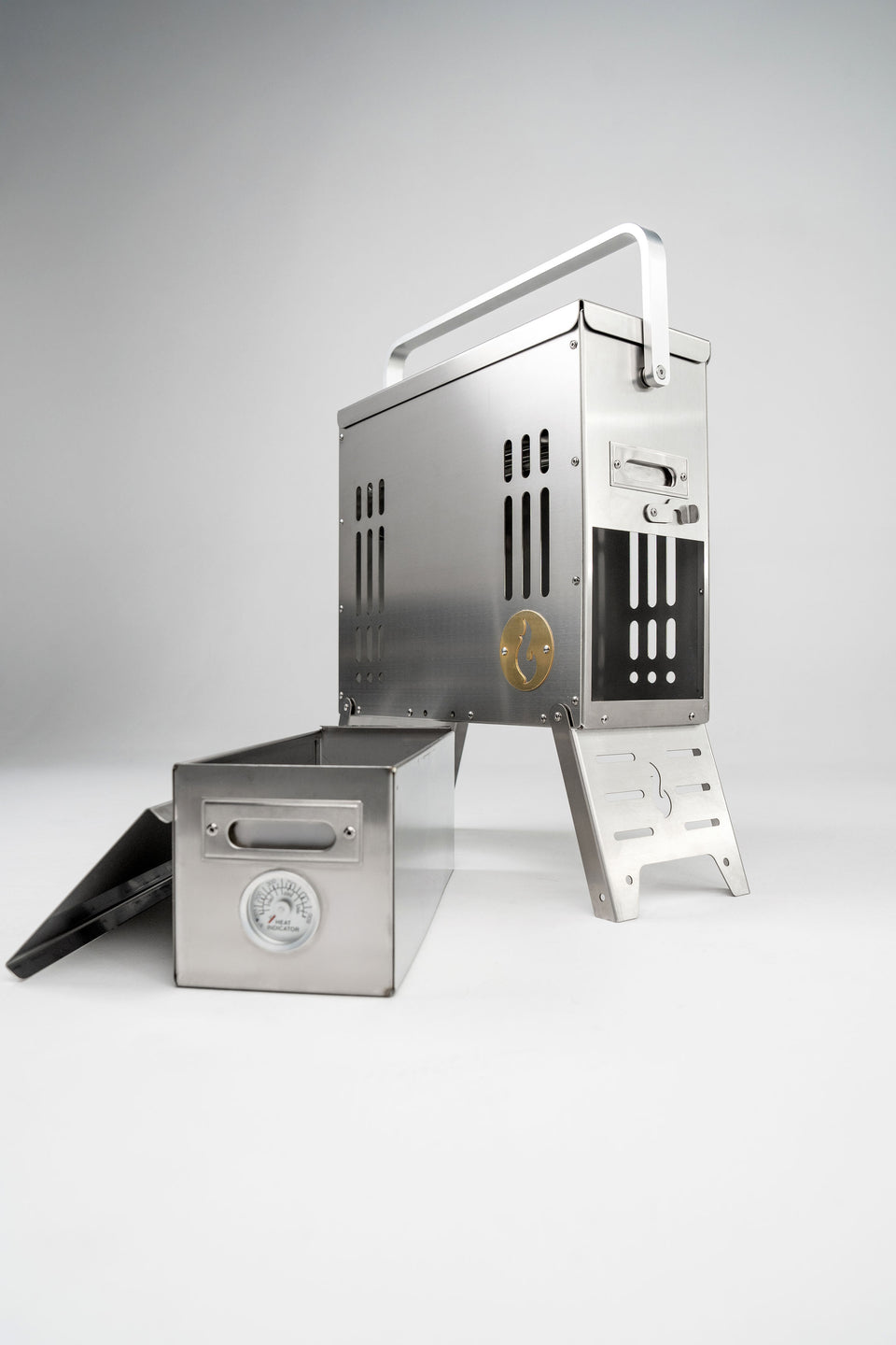 The LavaBox BoomBox Portable Campfire is a stainless steel grill with a handle and metal box featuring a built-in thermometer, offering dual-flame, smokeless campfires anywhere.