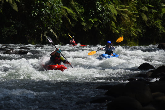 Three kayakers navigate through turbulent waters surrounded by lush greenery, showcasing the skills refined during the Costa Rica Paddling Trip with 4CRS Paddle School.