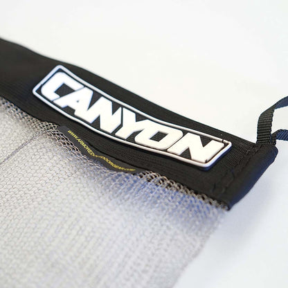 A stainless mesh drag bag from Canyon Coolers, ideal for outdoor adventures. The translucent black mesh and secure Velcro seal keep belongings safe. The bag is laid flat on a white background.
