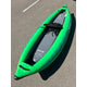 A green inflatable kayak, a used Demo STAR Raven Solo by NRS, is parked on an asphalt surface with a grey paddleboard labeled "STAR" stored inside. This rental demo boat also comes with a convenient carry bag.