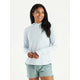 A woman wears the Free Fly Elevate Hoodie W's in light blue with drirelease tech and green shorts, standing against a plain white background, smiling and looking off to the side.