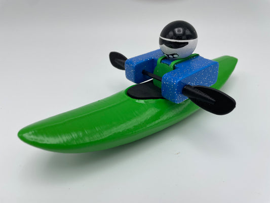The Foamie Mini Creeker from the Foamie Friends collection showcases a kayaker in a green boat wearing a blue outfit, expertly using black paddles to navigate through the water, making it ideal for river play adventures against a plain background.