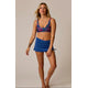 A woman stands against a neutral background in the Carve Hoku Swim Skirt with adjustable hem and a colorful floral bikini top, showing a relaxed expression and a gentle lean.