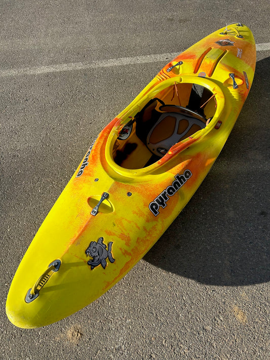 A Jackson Kayak Consignment Pyranha Burn MD kayak, suitable as a beginner boat, is parked in a parking lot.