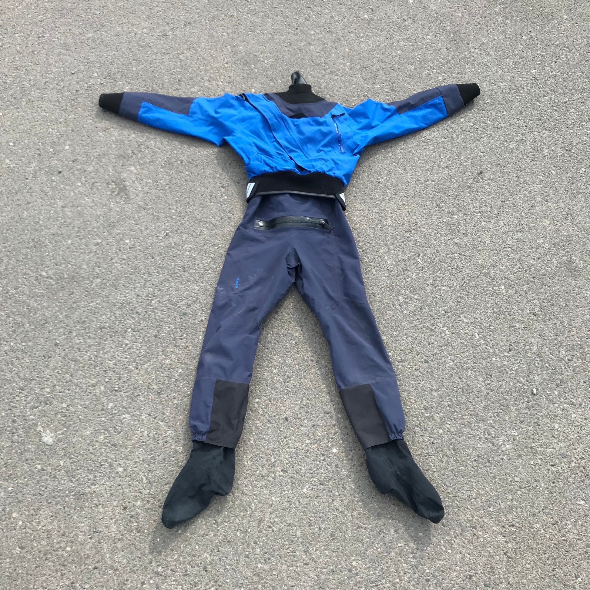 A man wearing a Kokatat Demo NRS GoreTex Axiom Drysuit Men's XL laying on the ground.