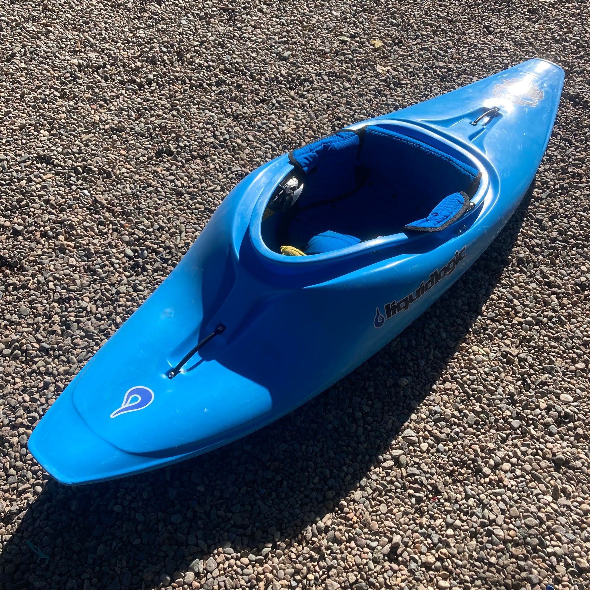 A blue LiquidLogic kayak sitting on gravel.