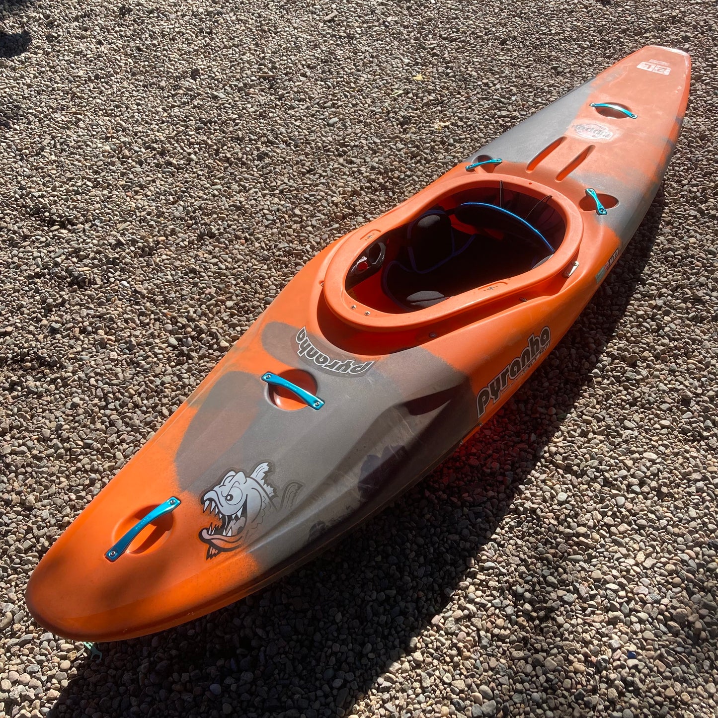 An orange and black Demo Ripper 2.0 LG kayak sitting on the ground, made by Pyranha.