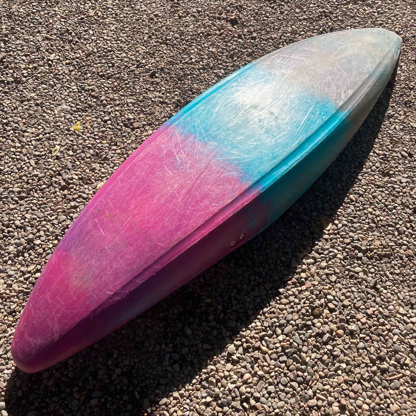 A Dagger Demo Rewind SM surfboard laying on the ground in a gravel area.
