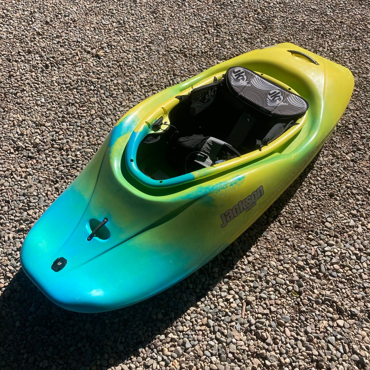 A yellow and blue Demo Rockstar V LG kayak sitting on gravel, made by Jackson Kayak.