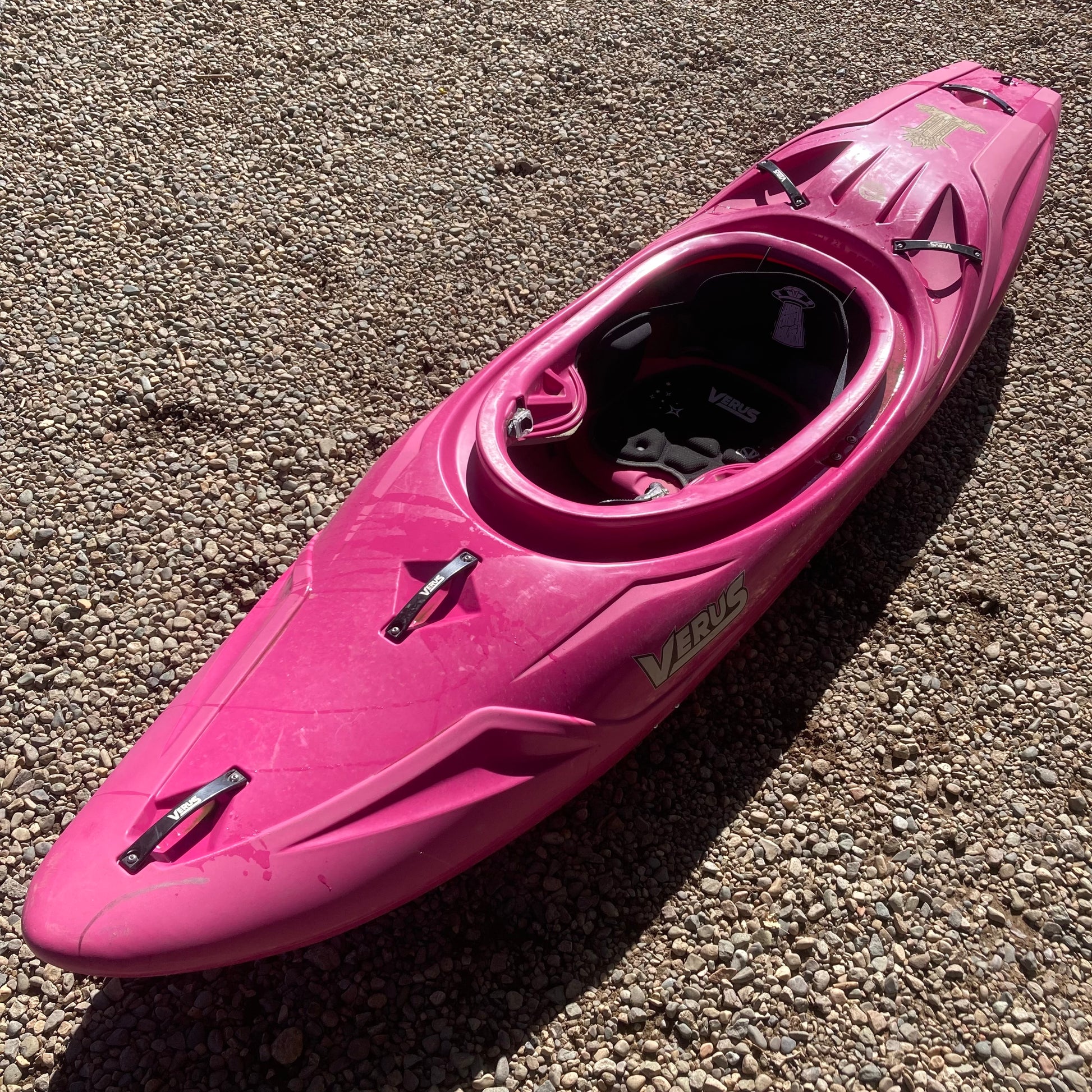 A pink Verus kayak laying on the ground.