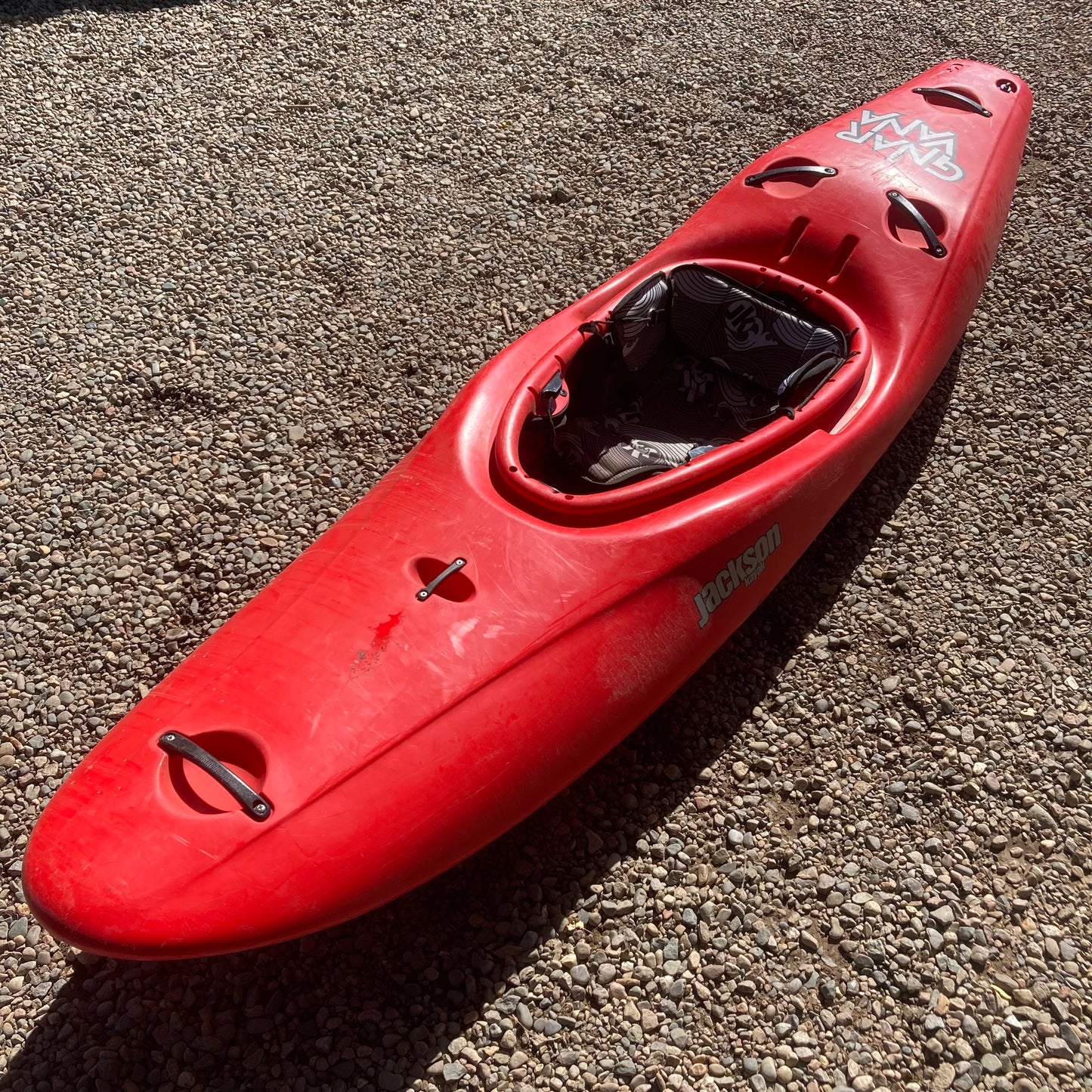 A red Demo Gnarvana SM kayak sitting on a gravel road.
