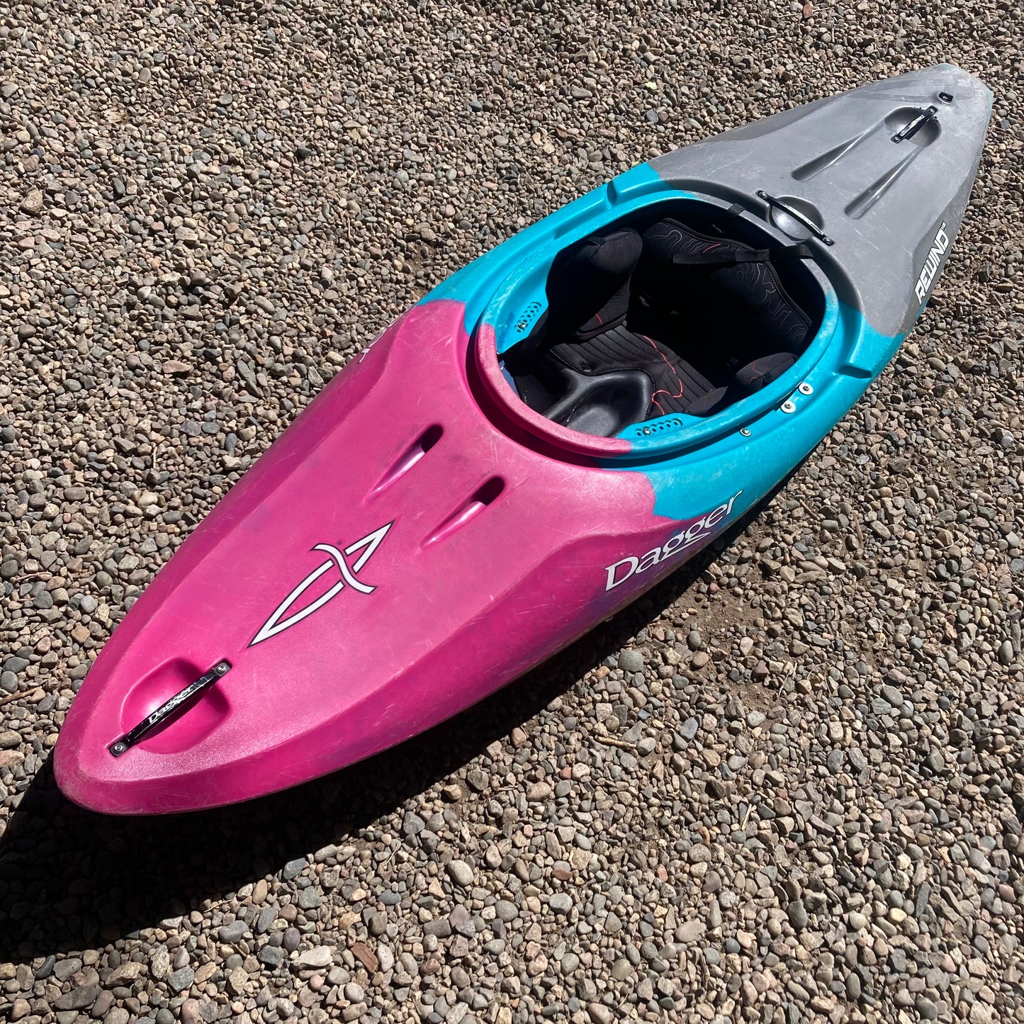 A pink and blue Dagger Demo Rewind XS kayak laying on the ground.