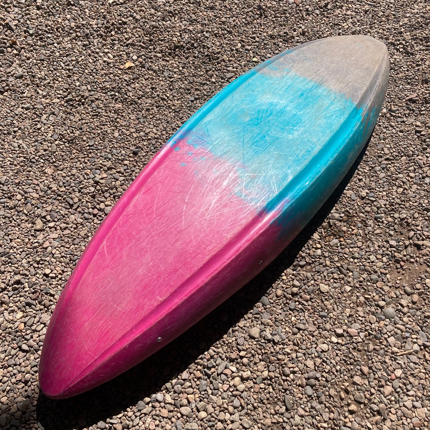 A blue and pink Demo Rewind XS surfboard by Dagger laying on the ground.