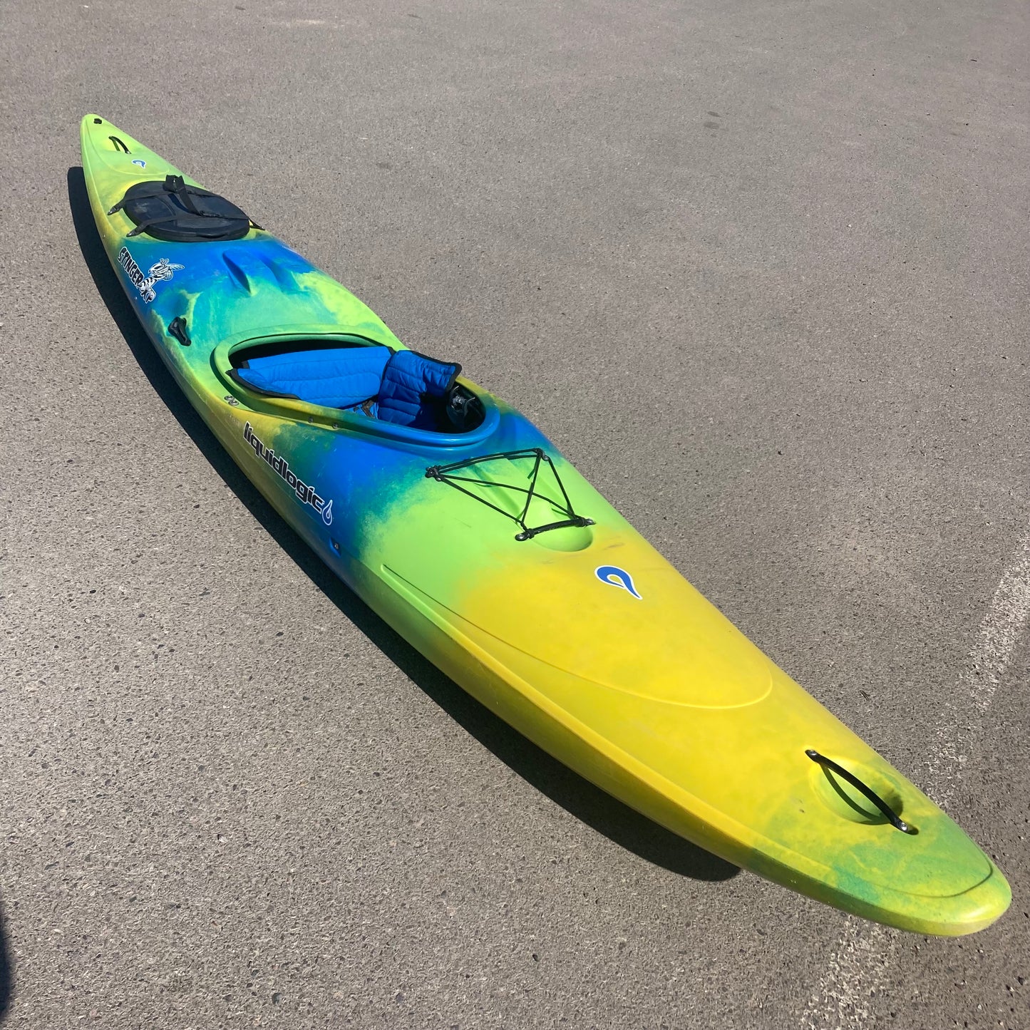 A yellow and blue LiquidLogic Demo Stinger XP kayak is parked in a parking lot.