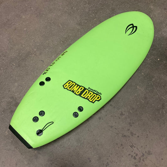 A Demo Bomb Drop surfboard by Badfish laying on a concrete floor.